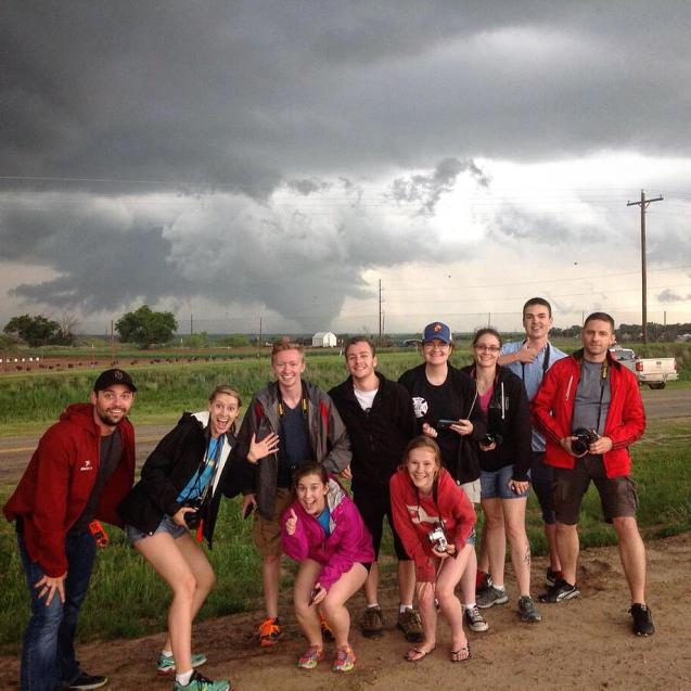 A class of students and professors posing in front of a giant tornado